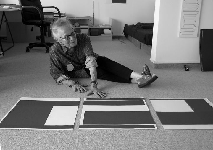 A picture showing Vera Molnar sitting on the floor in her atelier, working on some prints.